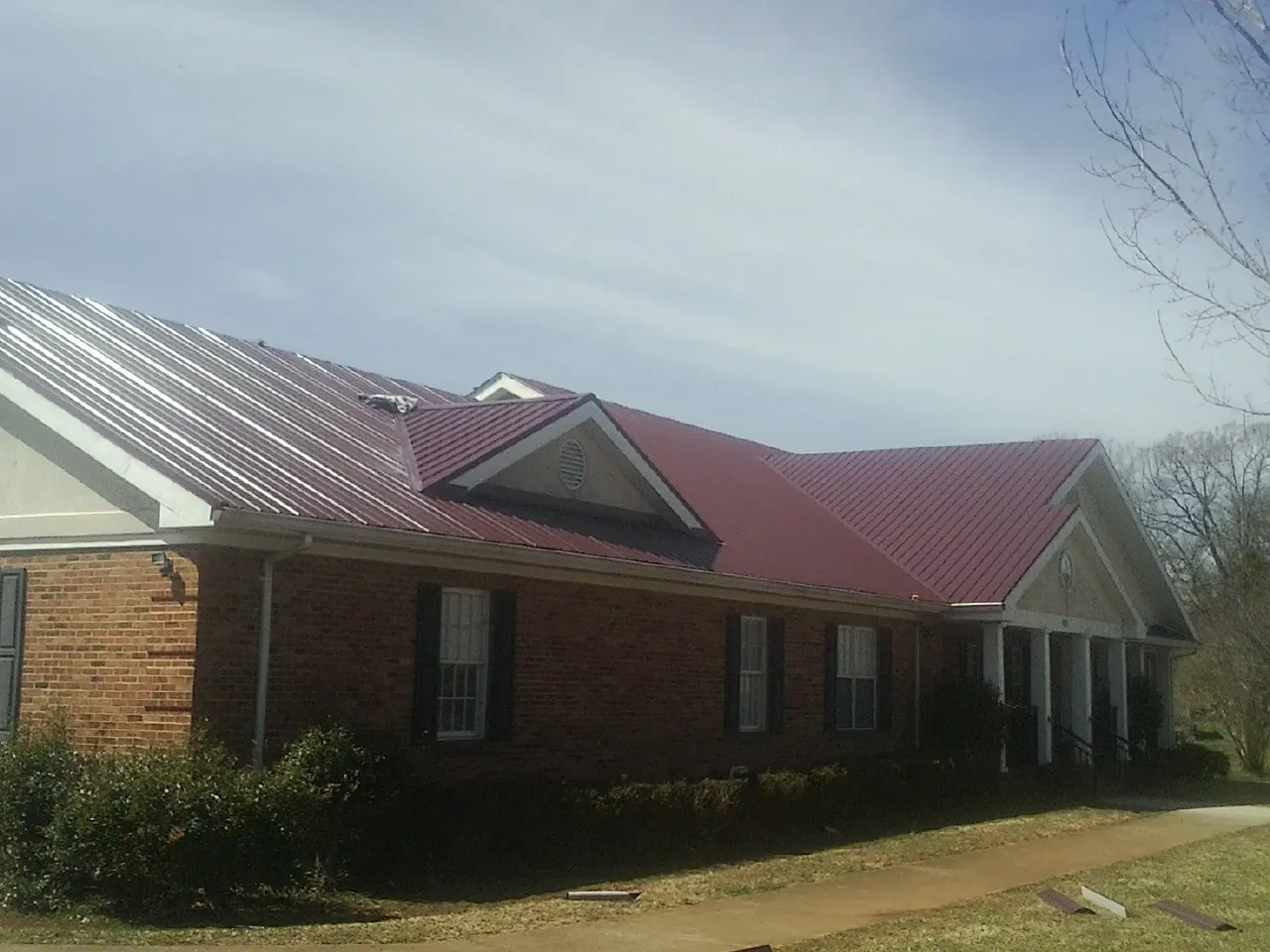 Red metal roof with gabled entries on a long brick building, from a Hail Damage Roof Repair job in Newark
